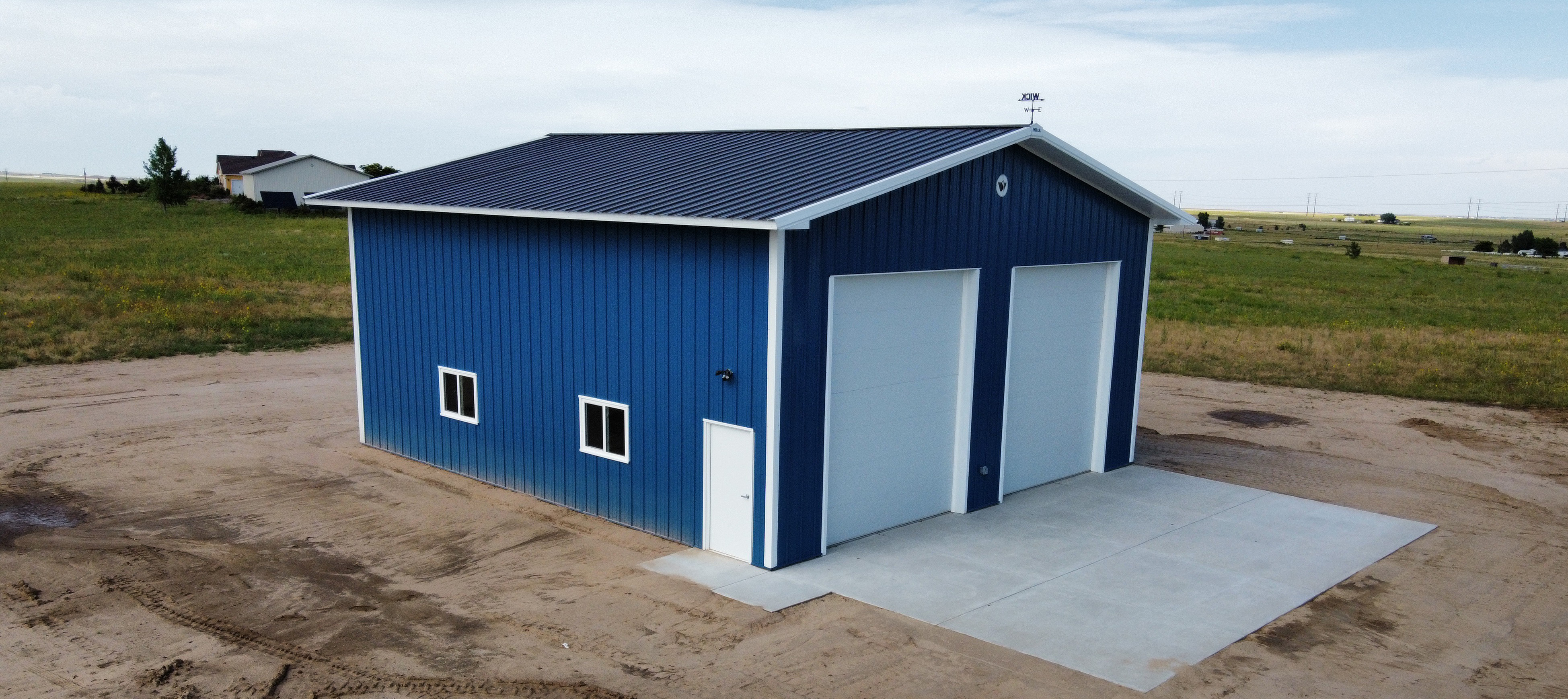 Blue post frame suburban building with white trim and two large, white garage doors